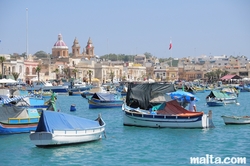 Luzzu in the harbour of Marsaxlokk and the parish church in the background