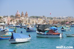 Luzzu in the harbour of Marsaxlokk and the parish church in the background Luzzu in the harbour of Marsaxlokk and the parish church in the background